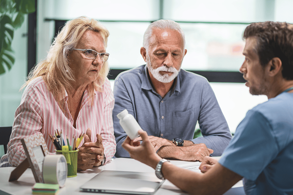 two older adults being handed a prescription bottle by a doctor